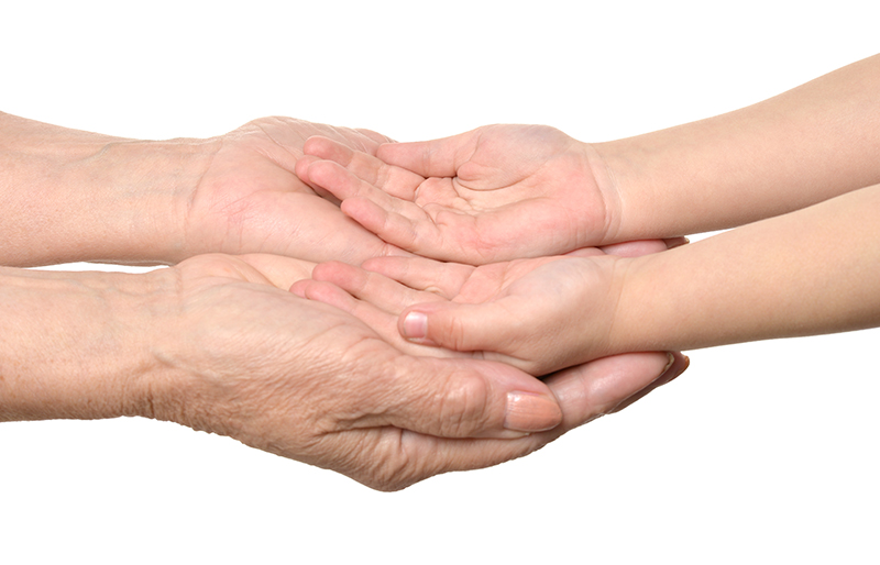 Older hands cupping younger hands, illustrating the contrast in skin aging and the need for hand rejuvenation.
