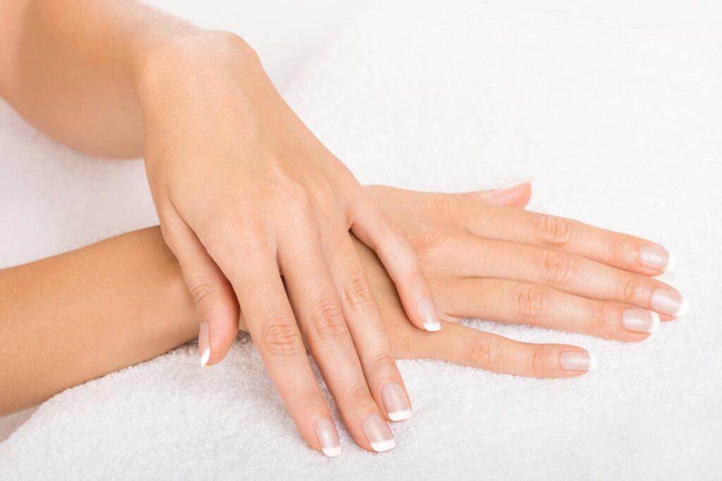 A pair of youthful, smooth hands with a classic French manicure resting gracefully on a soft white towel.