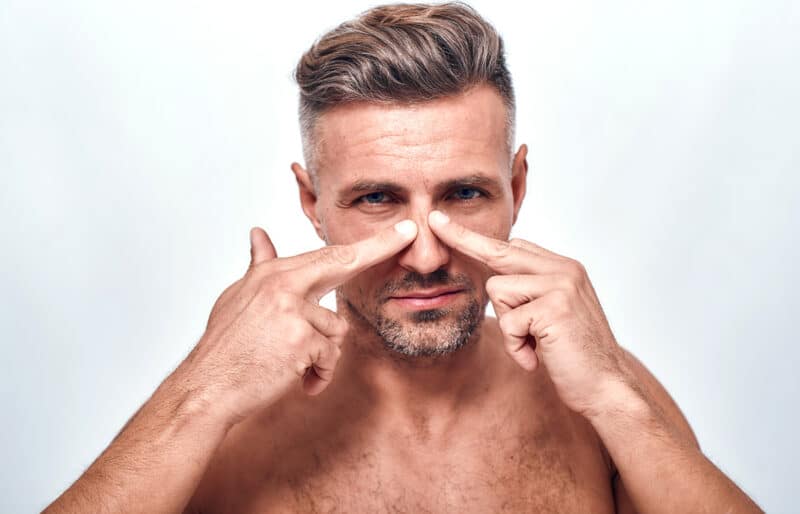 Man touches his nose, indicating the personal impact of rhinoplasty on men's self-esteem and identity.