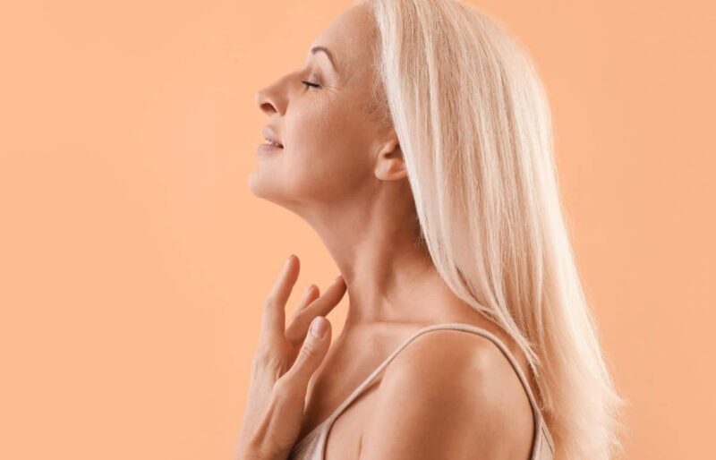 Mature woman with smooth jawline and firm neck skin, representing results of a surgical neck lift compared to alternatives.