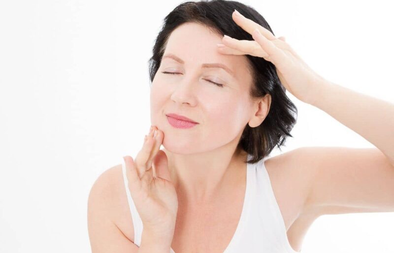 Middle-aged woman gently touching her face and neck, illustrating skin rejuvenation from neck lift procedure.