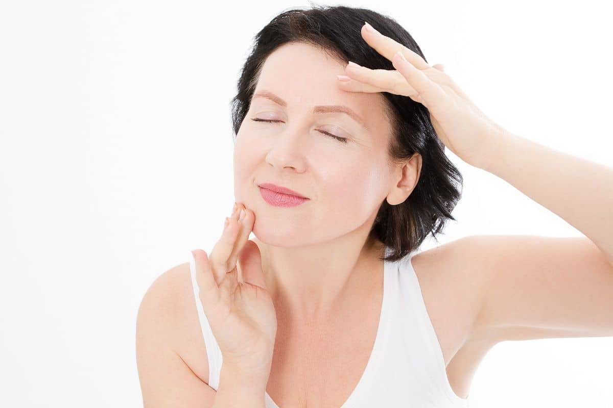 Middle-aged woman gently touching her face and neck, illustrating skin rejuvenation from neck lift procedure.