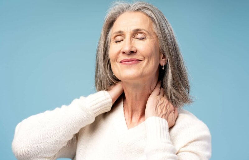 Woman gently holding neck with eyes closed, representing neck lift recovery and improved jawline contour